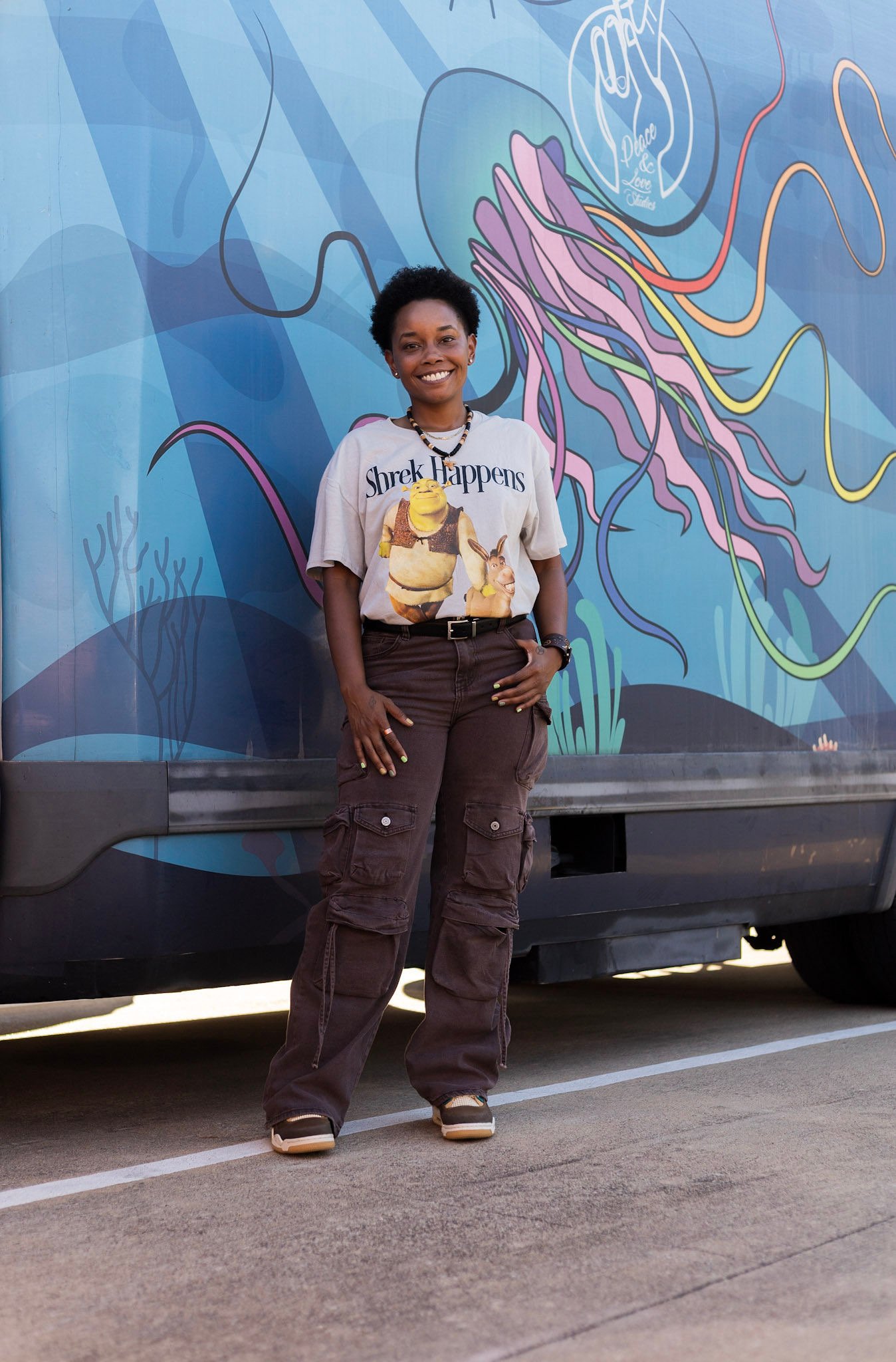 Jelly Robinson standing in front of her mobile Peace & Love Studio truck, painted with a jellyfish and peace-sign hand mural